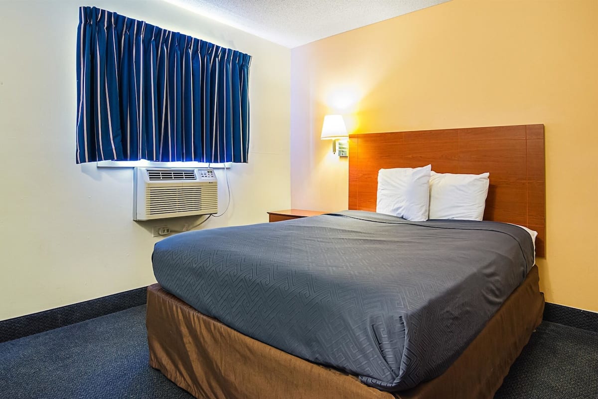 Een hotelkamer met een bed, nachtkastje, lamp en een airconditioning.