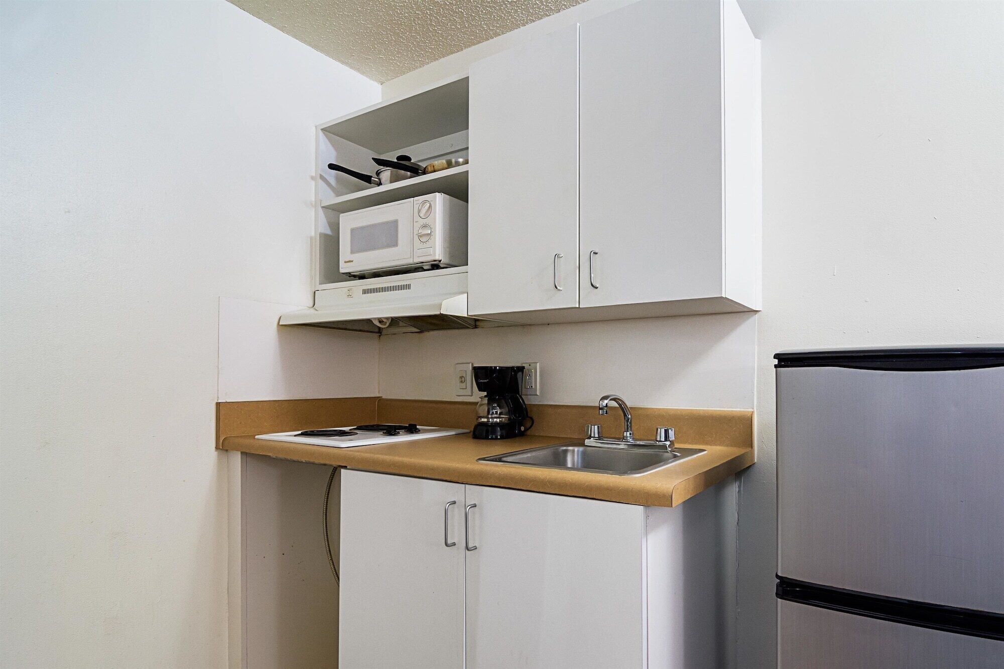 A compact kitchenette with a microwave, coffee maker, and a stainless steel refrigerator.