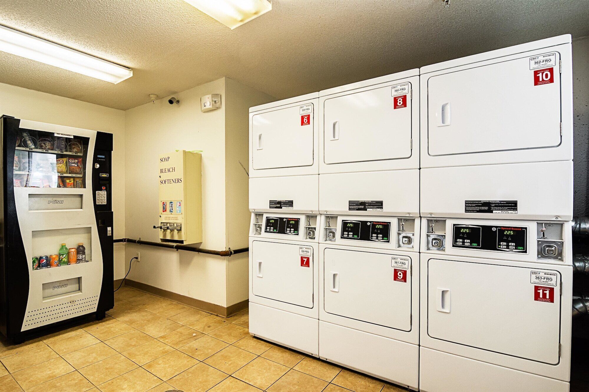 A laundry room with multiple washers and dryers, a vending machine, and a soap and bleach dispenser.