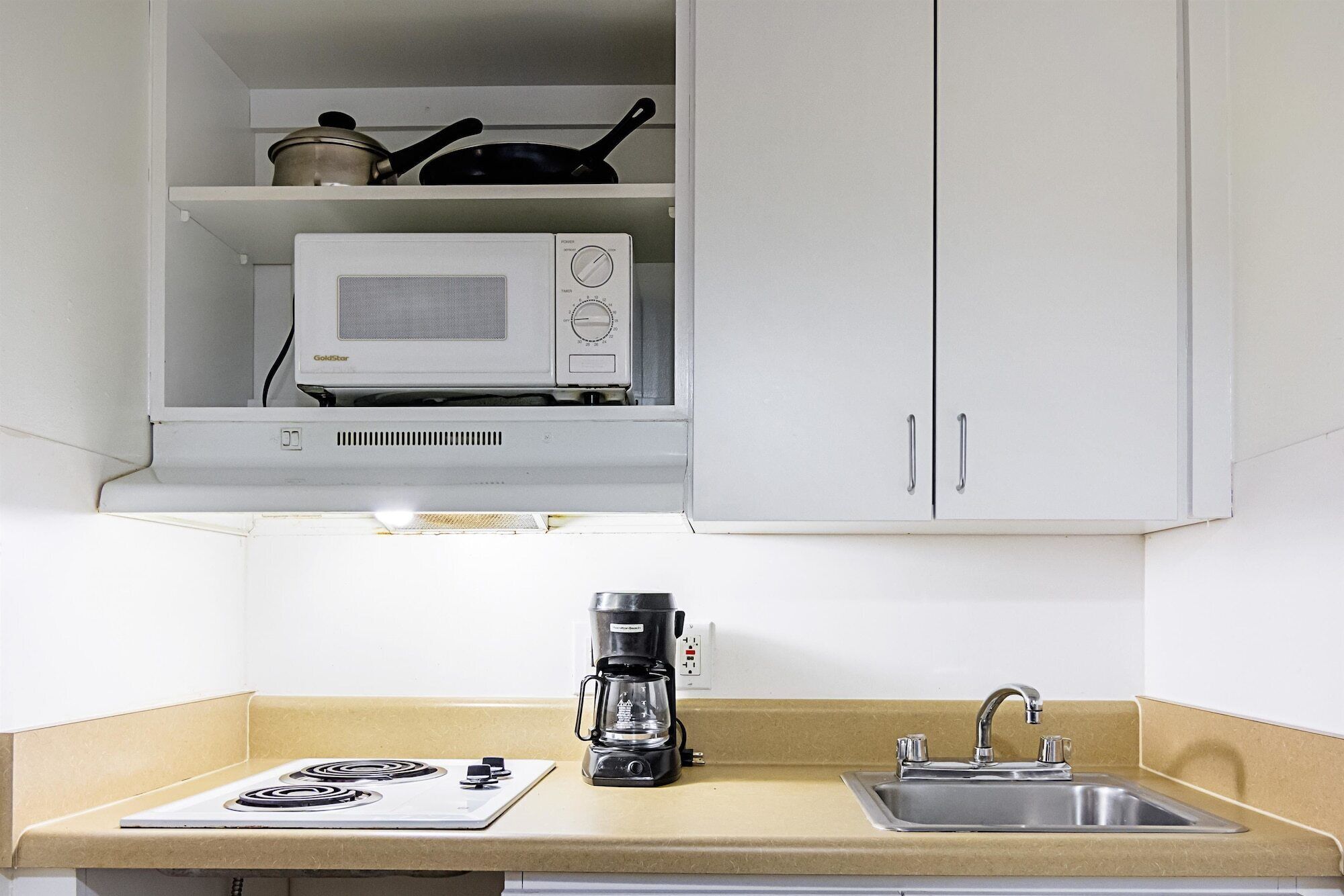 A compact kitchenette with a microwave, a coffee maker, a sink, and a stove.
