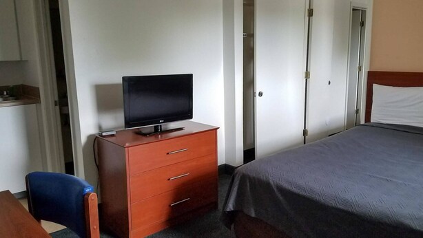 A hotel room with a bed, a TV on a wooden dresser, a desk with a chair, and a wardrobe. - Motel 6 - Fayetteville, NC - Fort Liberty Area (Fayetteville)