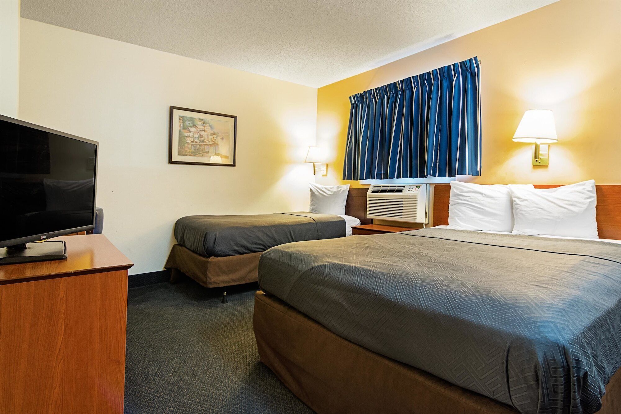 A hotel room with two beds, a TV, a painting, and a window with curtains.