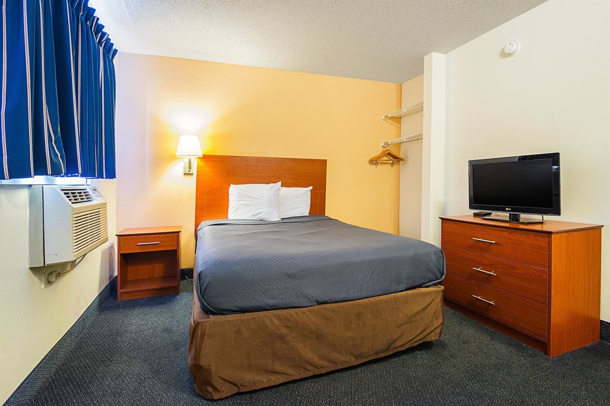 Habitación de hotel con cama, televisor, cómoda de madera, mesita de noche y un calentador instalado en la pared.