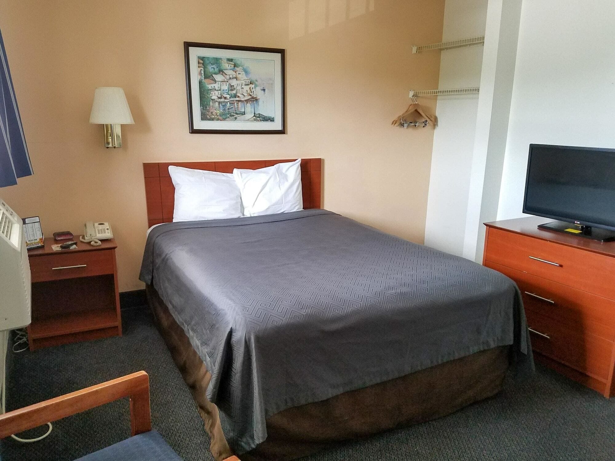 A hotel room with a bed, a desk with a lamp, a television, and a painting on the wall.