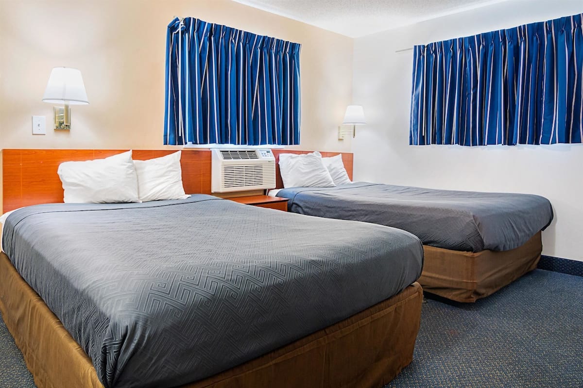 Een hotelkamer met twee bedden, een houten hoofdbord, een airconditioner bevestigd aan de muur en blauwe gordijnen.