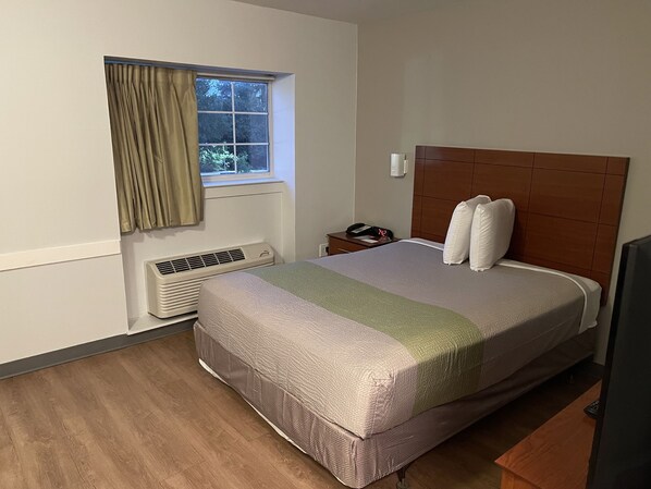 Habitación de hotel con una cama grande, una mesita de noche con teléfono, una ventana con cortinas y un calentador instalado en la pared.