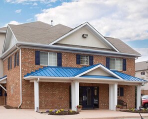 A two-story brick house with a blue roof, a front porch, and a small garden area. - Motel 6 Richmond, VA - I-64 West (Richmond)