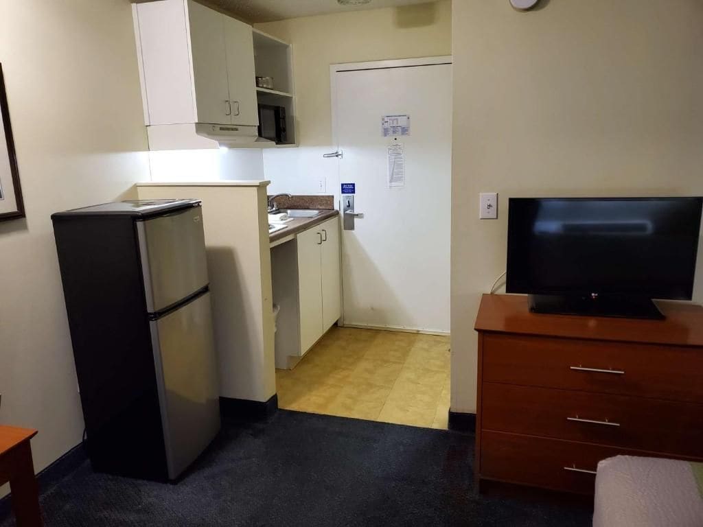 A compact room with a kitchenette, a television, and a small table.