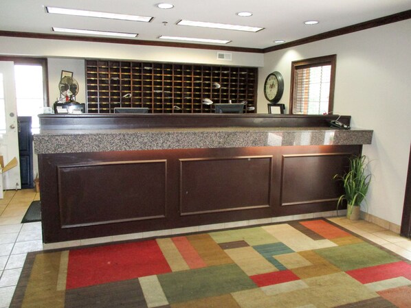 A reception area with a check-in counter, a clock, and a patterned carpet. - Motel 6 Richmond, VA - I-64 West (Richmond)