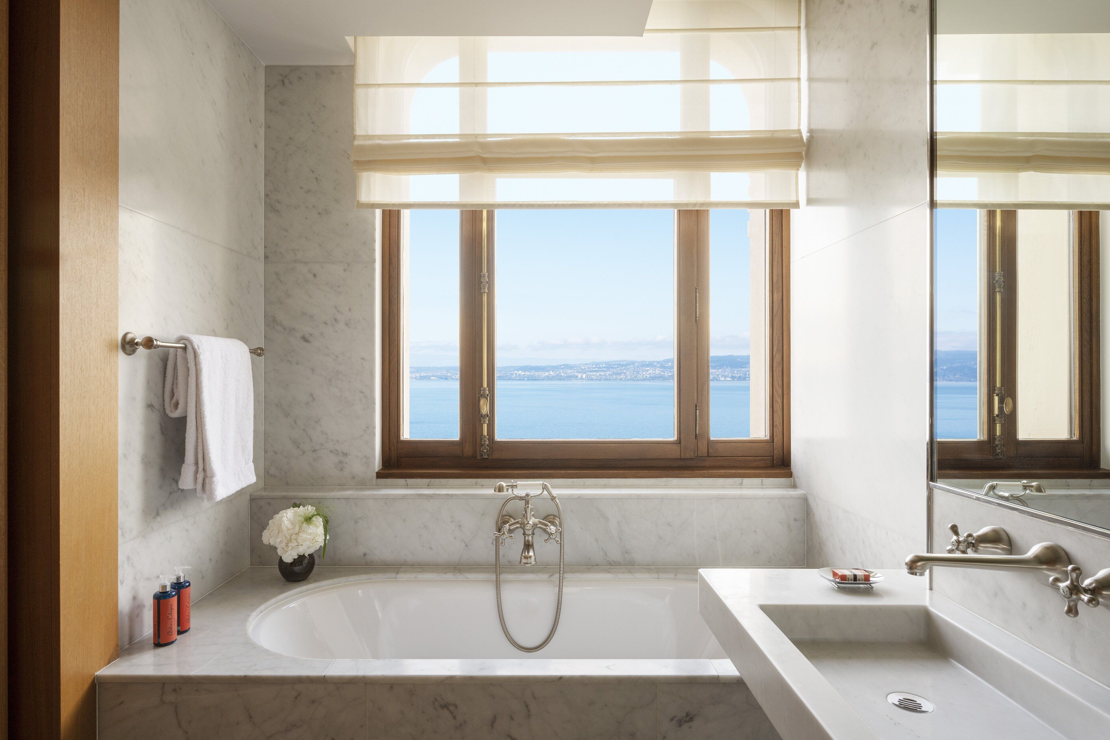 A bathroom with a large bathtub, a sink, and a window with a view of the sea.
