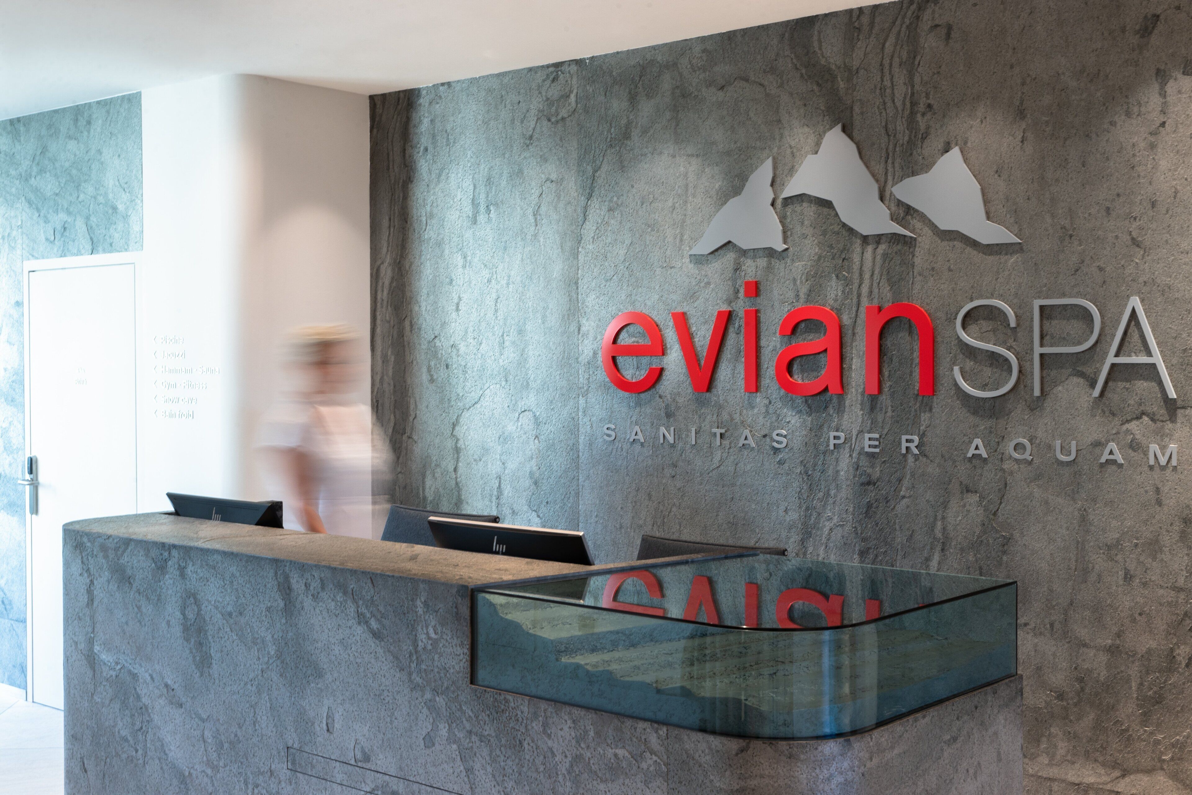 A reception desk with a modern design, featuring a glass partition and a logo for 'evian SPA'.