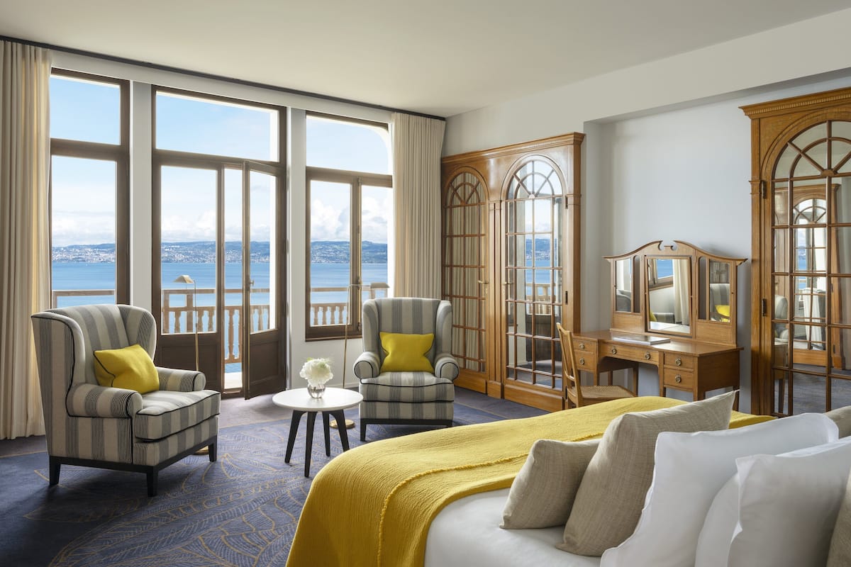 Een hotelkamer met een groot raam, een bed, een bureau en twee fauteuils.