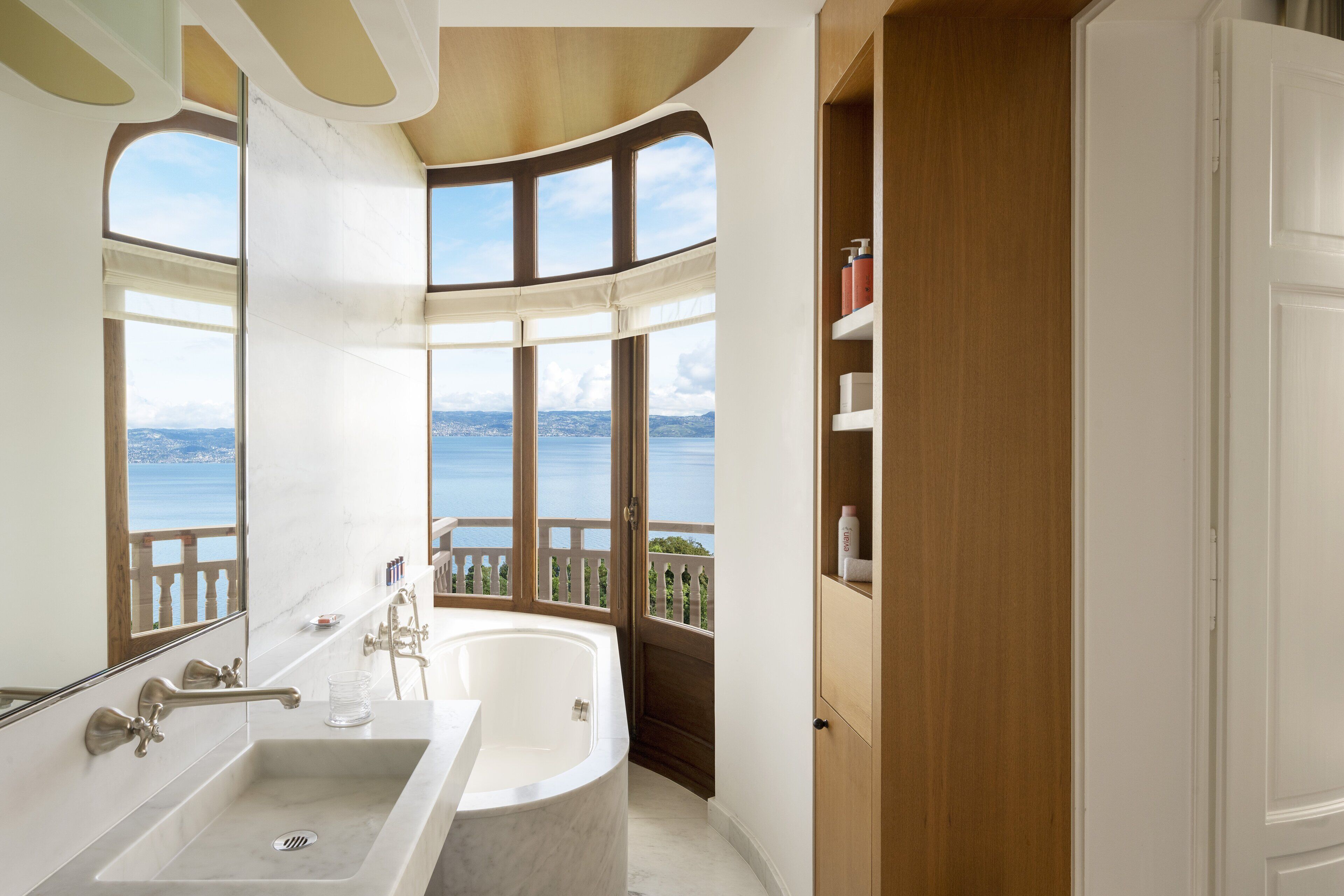 Ein Badezimmer mit einer großen Badewanne, einem Waschbecken und einem Fenster mit Blick auf ein Gewässer.