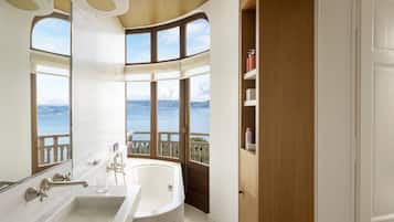 Ein Badezimmer mit einer großen Badewanne, einem Waschbecken und einem Fenster mit Blick auf ein Gewässer.