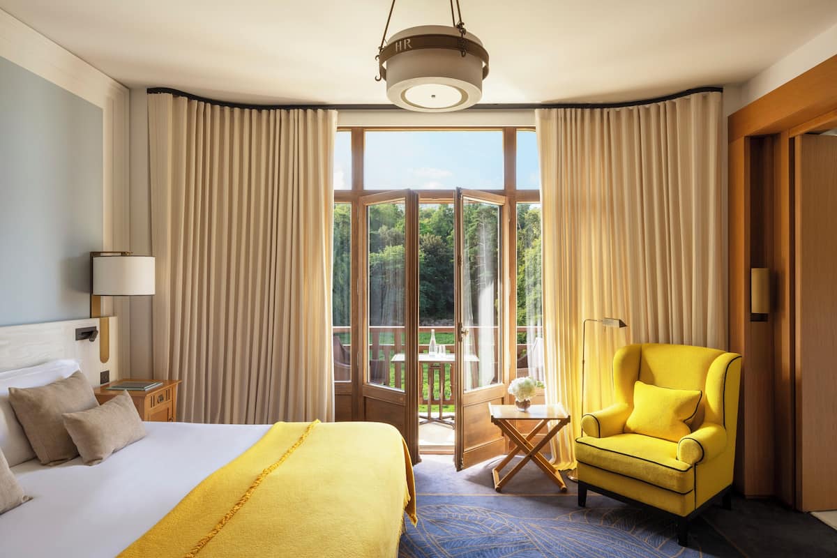 Een hotelkamer met een bed, een gele fauteuil, een balkon en gordijnen.