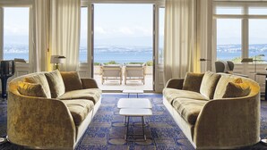 Un salon luxueux, doté d’un grand canapé, d’une table basse et offrant une vue sur la mer grâce à de grandes fenêtres.