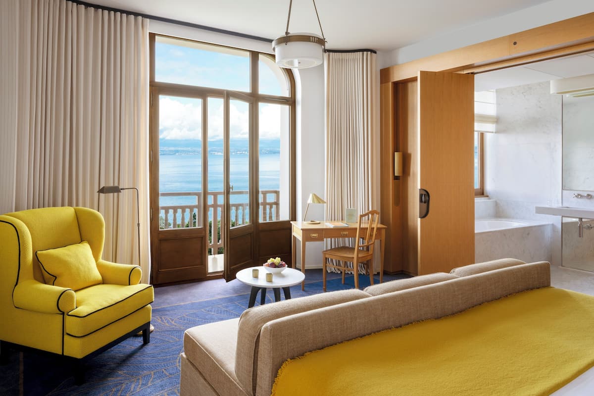 Een hotelkamer met een bed, een bureau, een stoel, een klein tafeltje en uitzicht op zee.