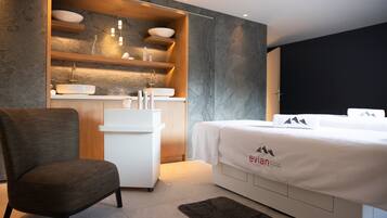 Una habitación de hotel moderna con una cama, una silla, un pequeño escritorio con lavabo y una estantería con artículos de aseo.