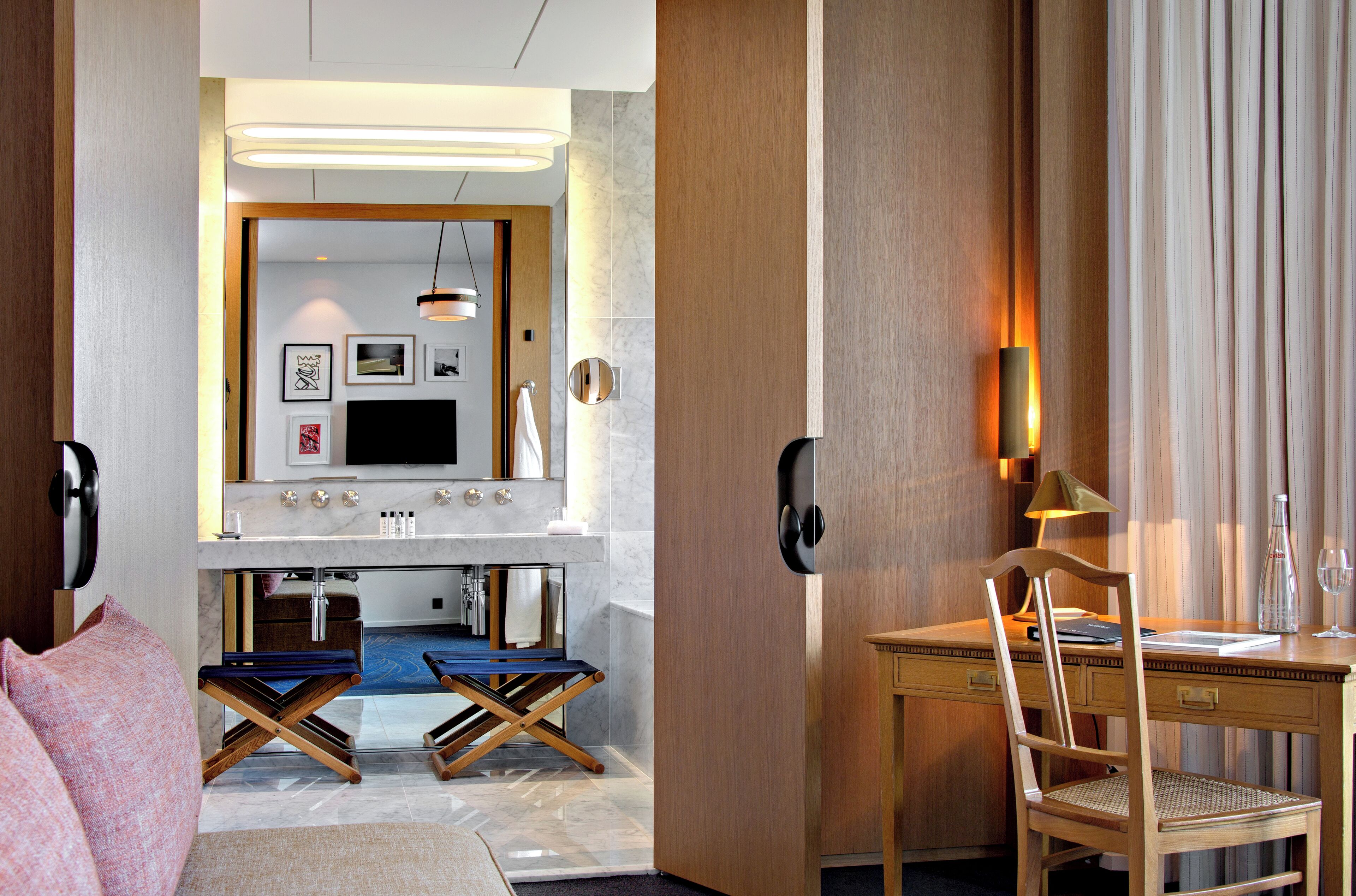 A modern hotel room with a wooden desk, a chair, a small table, a sofa, and a TV.