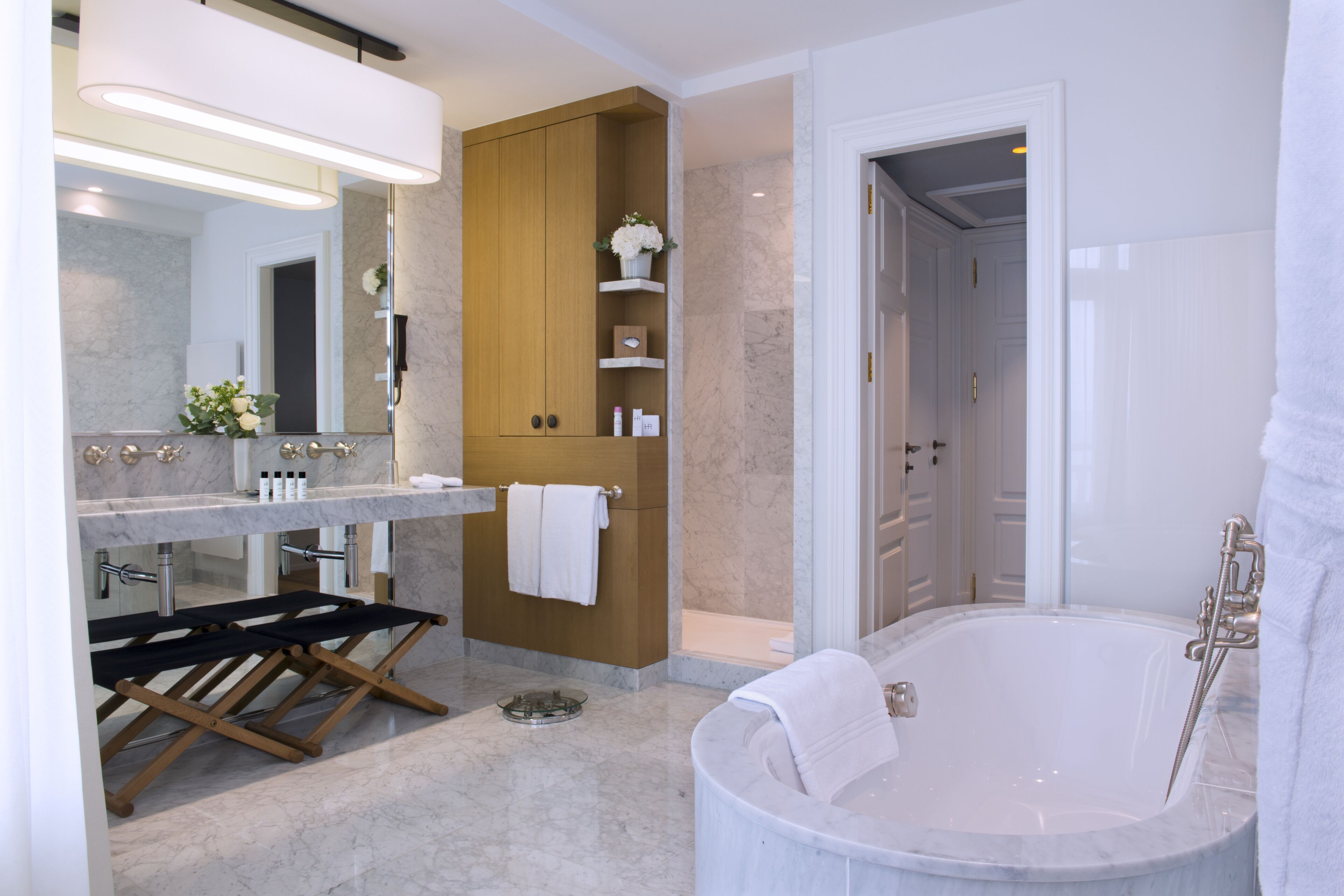 A modern bathroom with a marble sink, a freestanding bathtub, and wooden shelves.