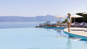 Zona de piscina con sillas de descanso y sombrillas, con vista a un cuerpo de agua y montañas.