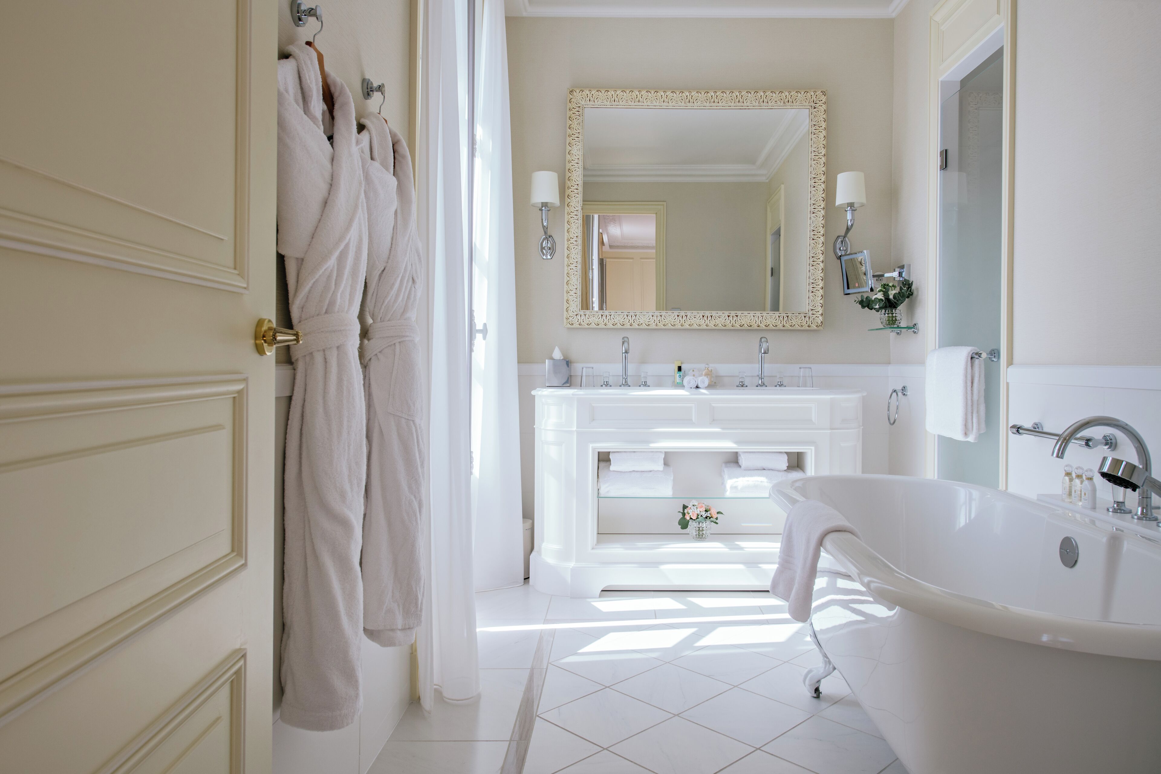 A spacious bathroom with a large bathtub, a double vanity with a mirror, and a door with hanging robes.
