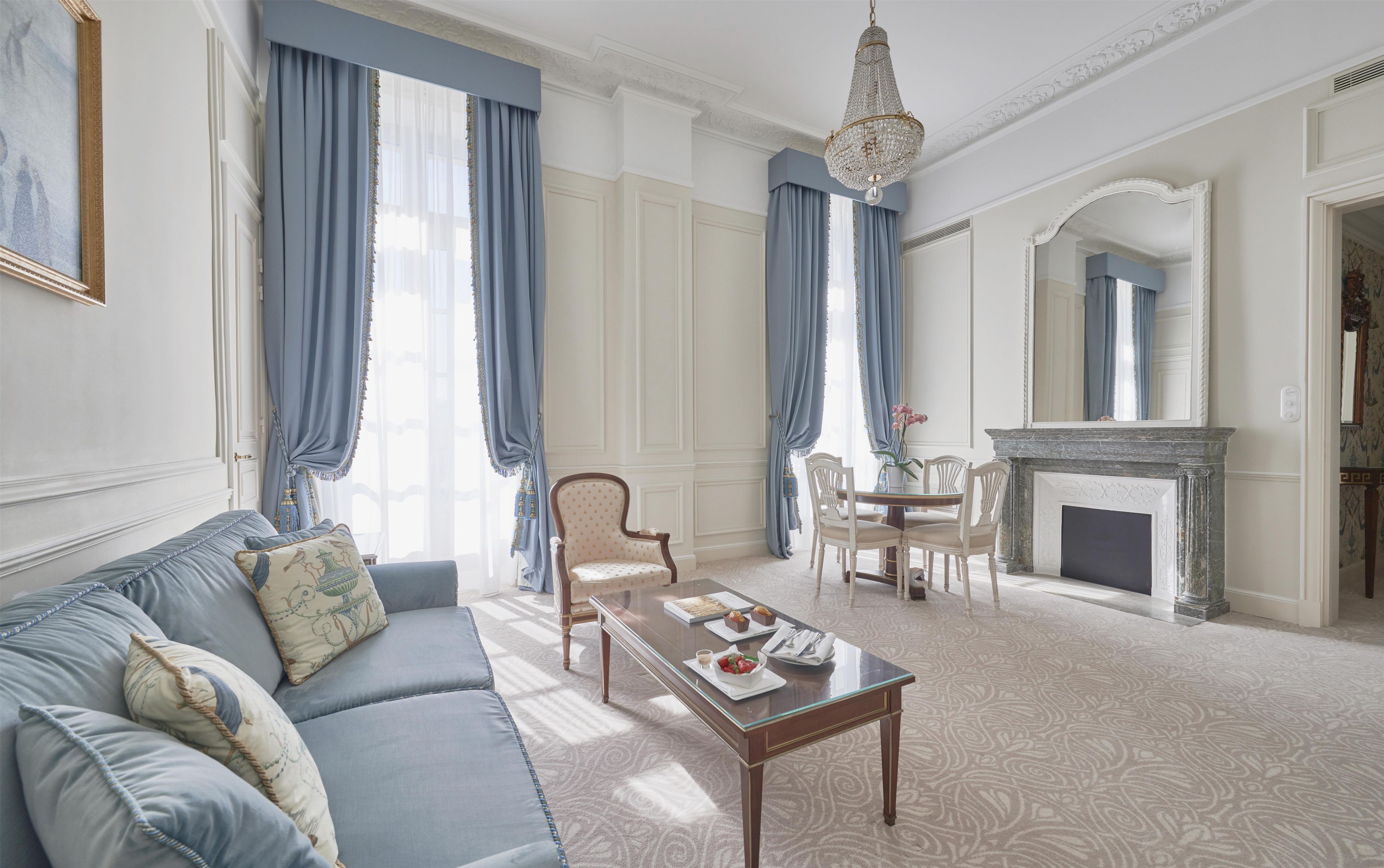 A room with a sofa, a dining table with chairs, a chandelier, a fireplace, and a large mirror.
