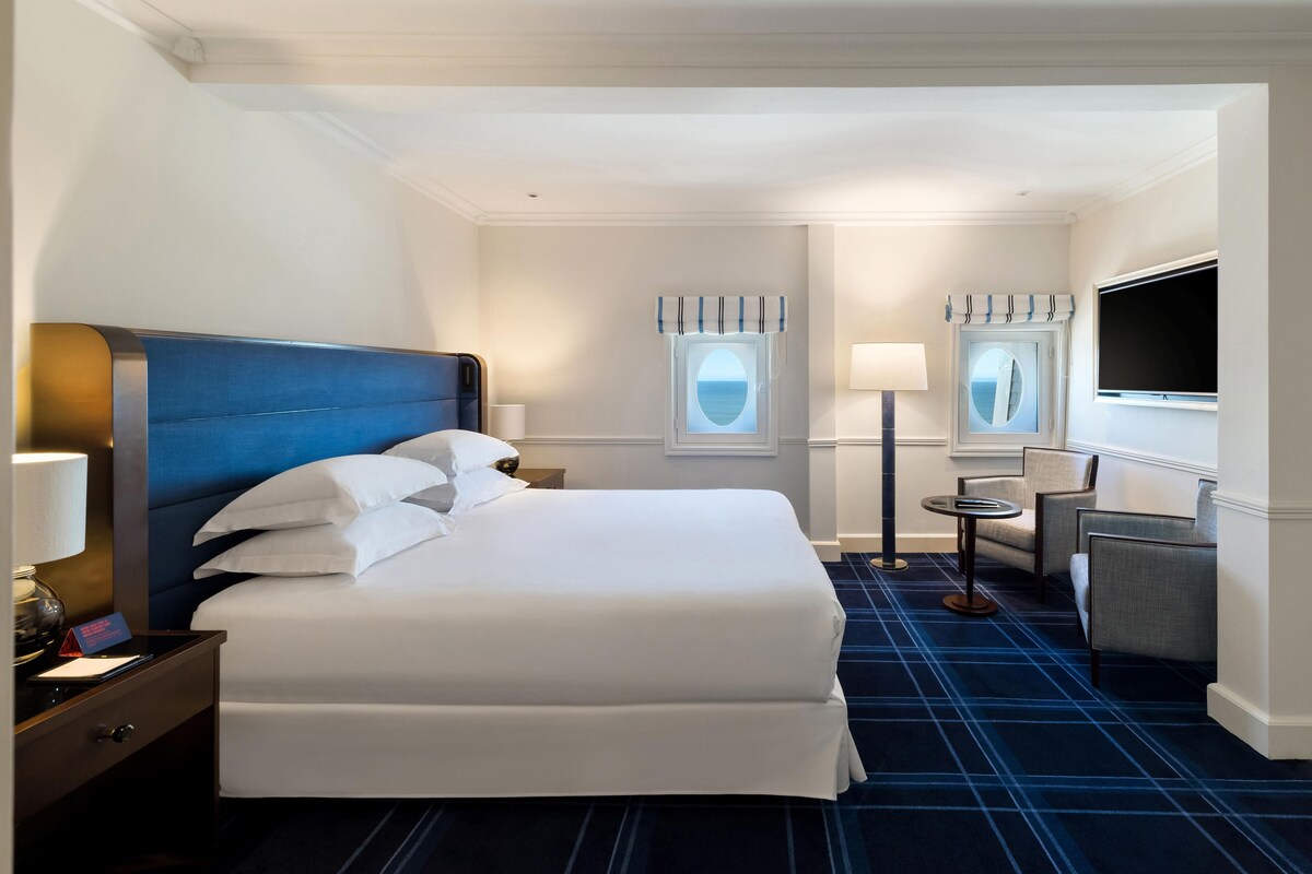 Hotelkamer met groot bed, nachtkastjes, bureau, stoel, televisie en raam met gordijnen.