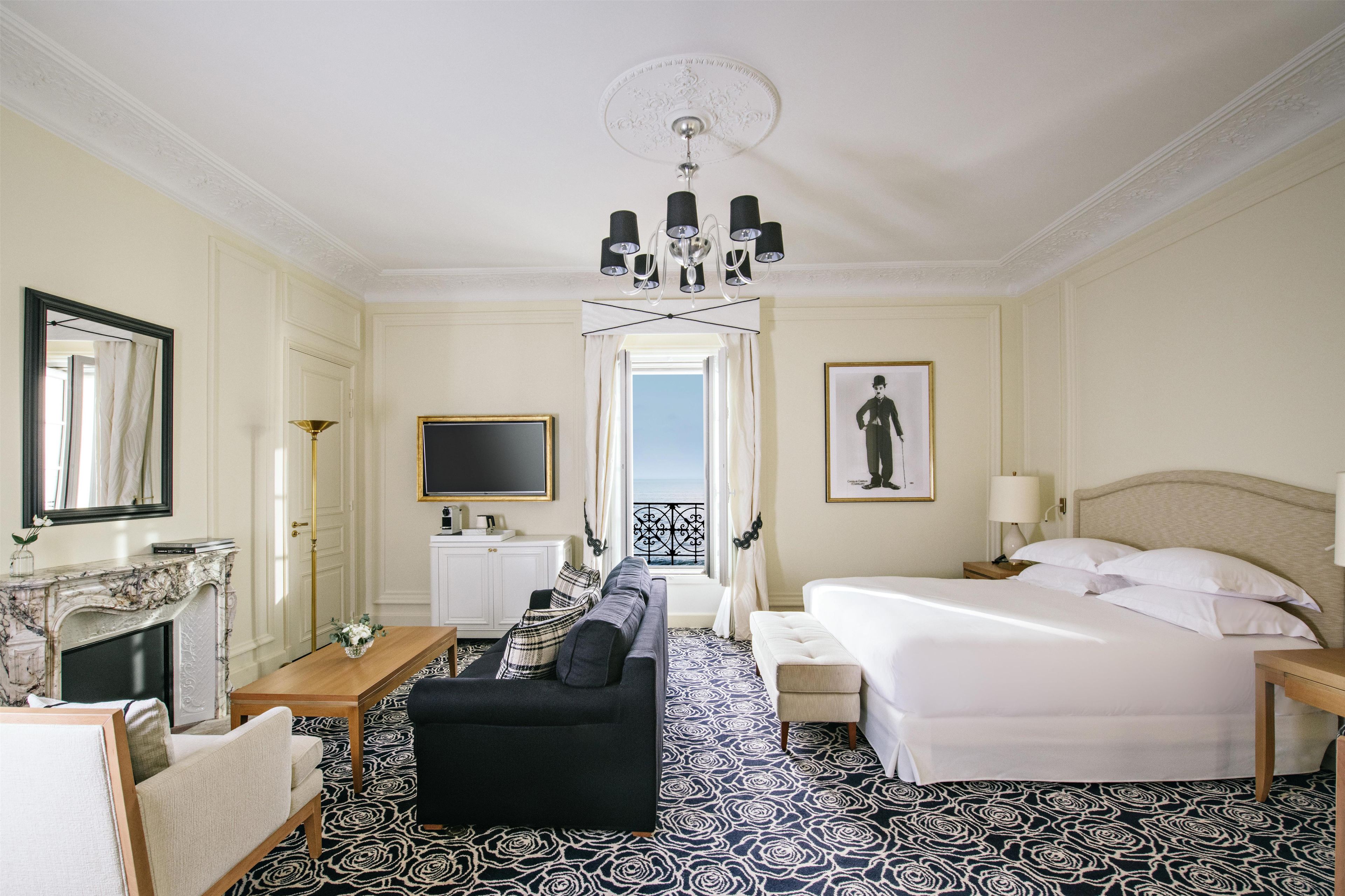 A hotel room with a sofa, a bed, a TV, a fireplace, and a balcony view.