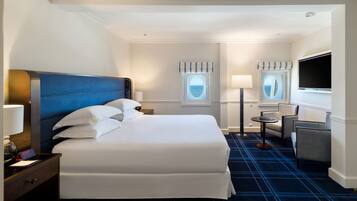 A hotel room with a large bed, a desk with a lamp, a chair, a TV, and a window with curtains.