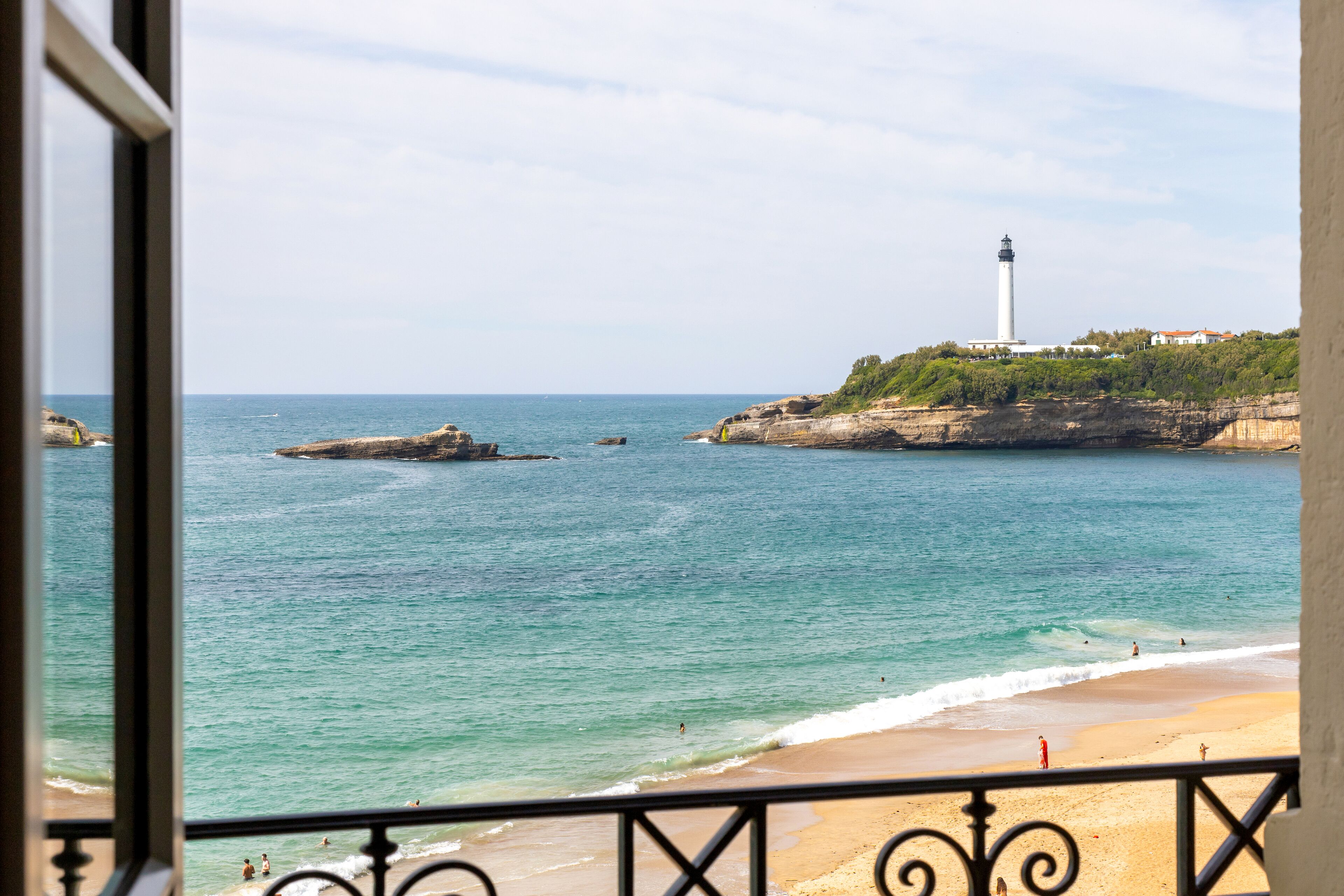 A coastal view with a lighthouse, beach, and rocky outcrops.