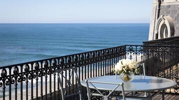 A balcony with a metal railing, a table with a vase of flowers, and a view of the ocean.