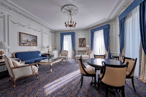 A room with a blue patterned carpet, a round dining table with chairs, a sofa, and two armchairs.