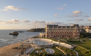 Un hotel frente al mar con una piscina grande, un faro y un edificio imponente de varias plantas.