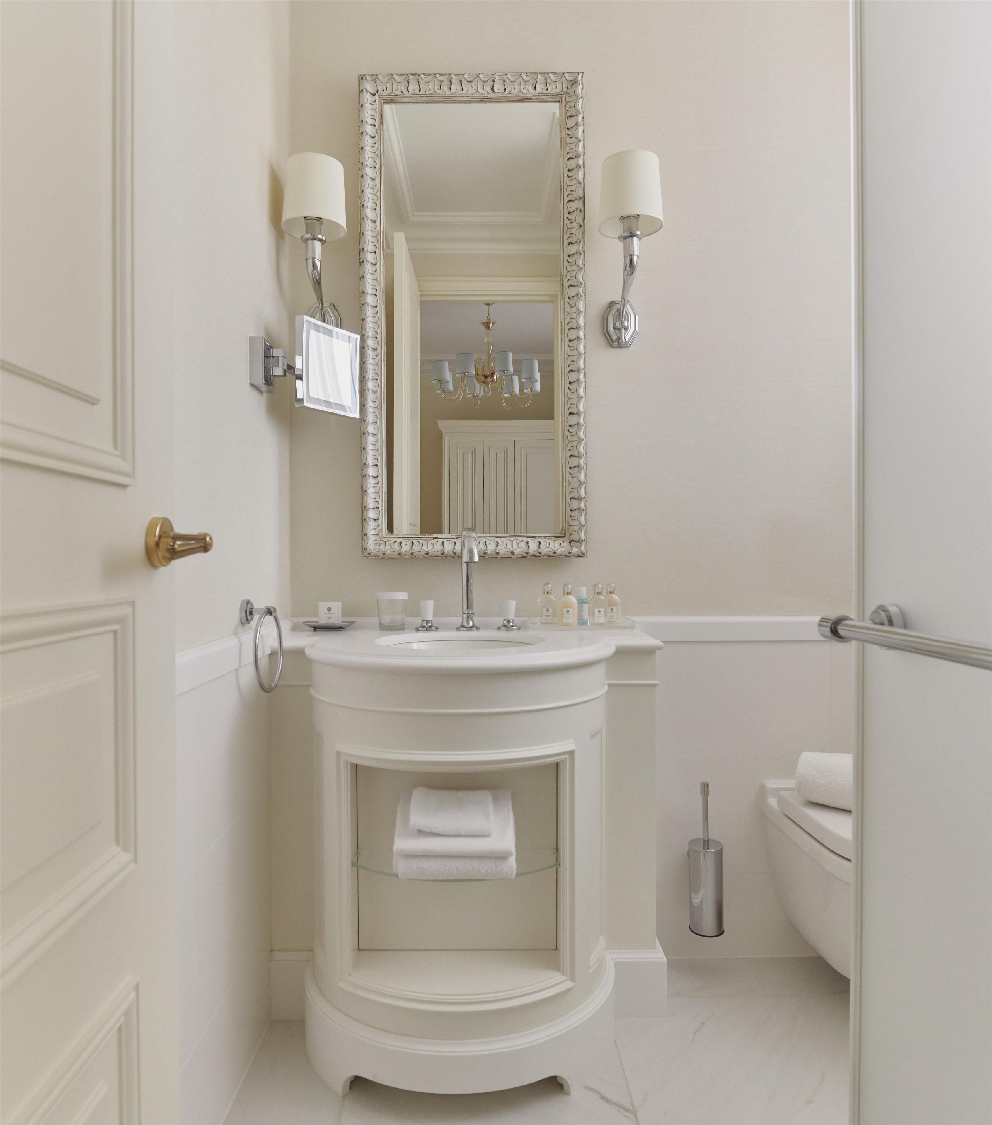 A bathroom with a white vanity, a large mirror, two wall-mounted lights, a towel rack, and a toilet.