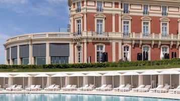 Un hotel con una amplia zona de piscina, tumbonas y una imponente fachada.