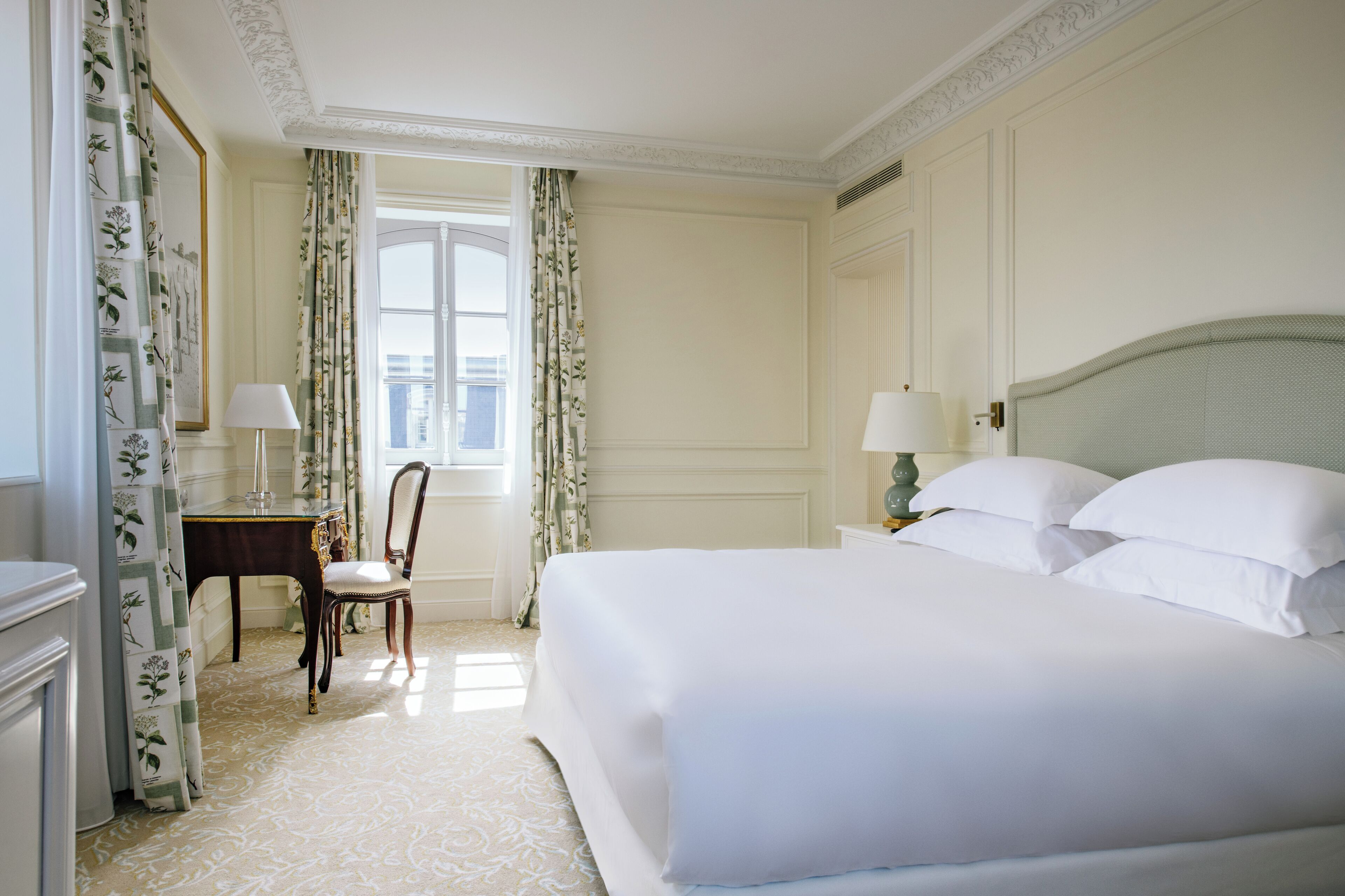 A hotel room with a large bed, a nightstand, a chair, a desk, and a window with curtains.