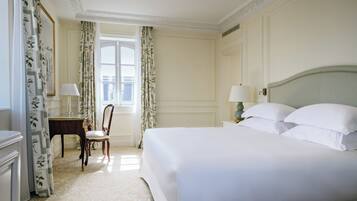 A hotel room with a large bed, a nightstand, a chair, a desk, and a window with curtains.