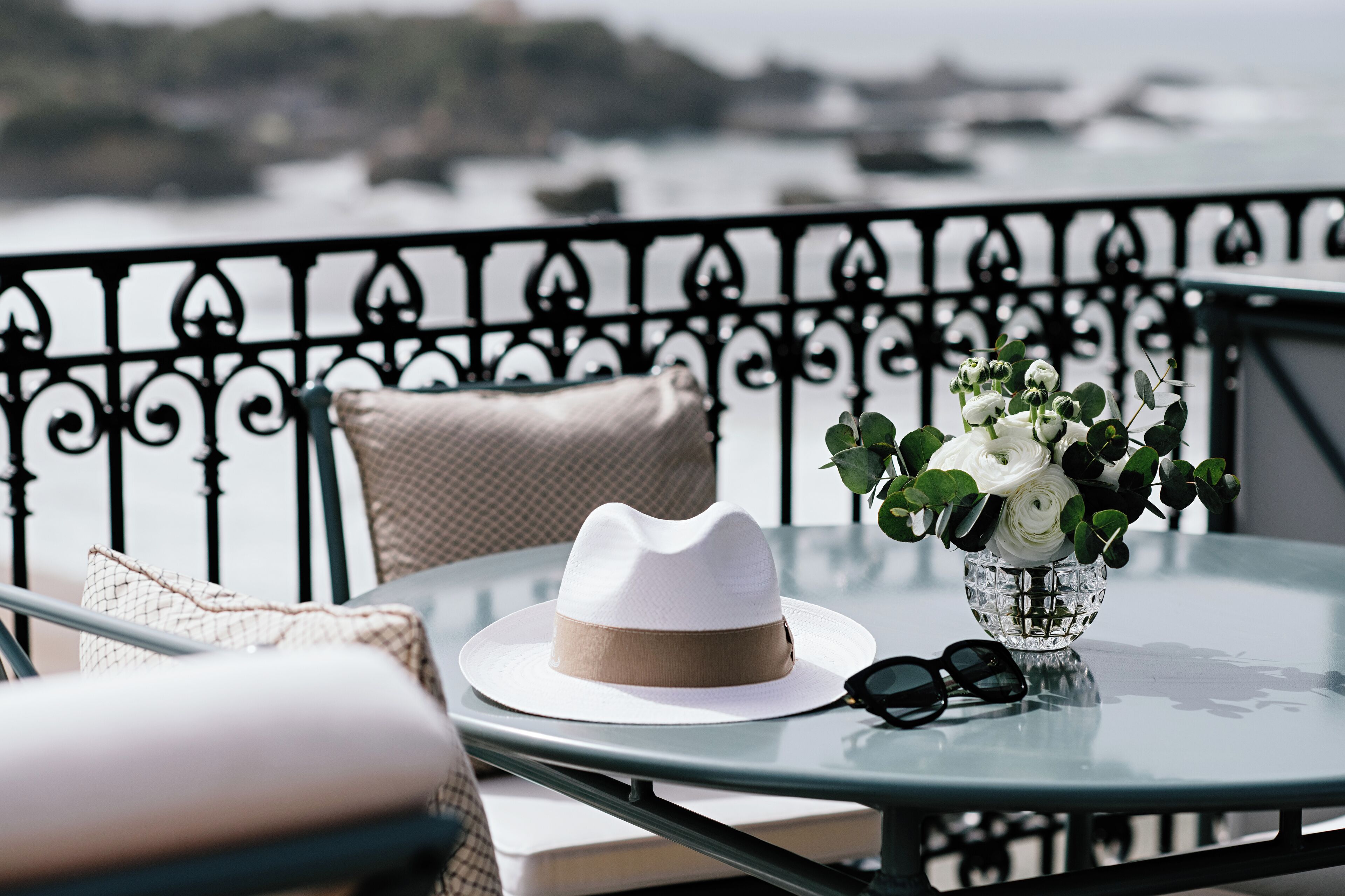 A table with a white hat, a vase with white flowers, and a pair of sunglasses.