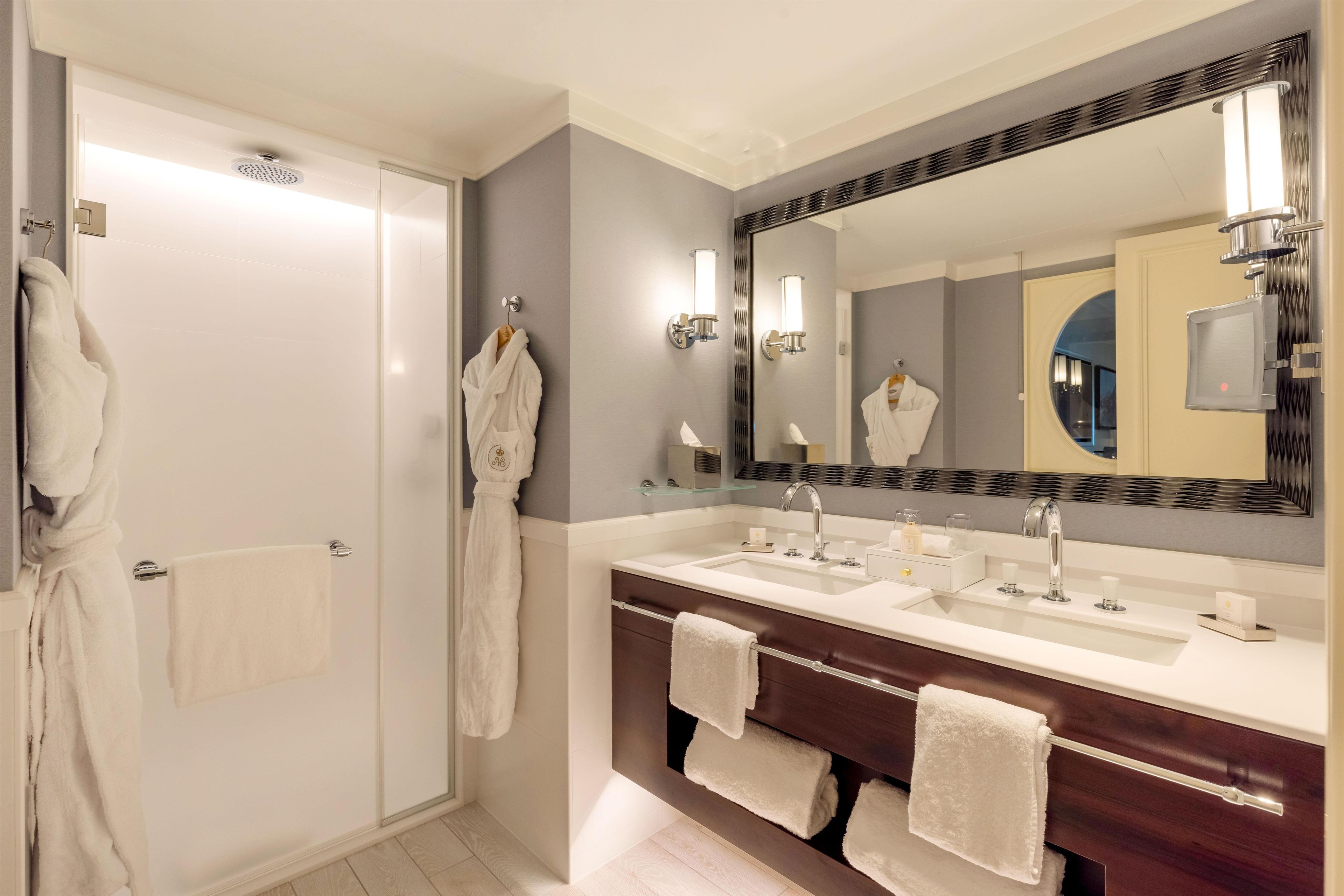 A hotel bathroom with a double sink vanity, a large mirror, and two towels hanging on the wall.