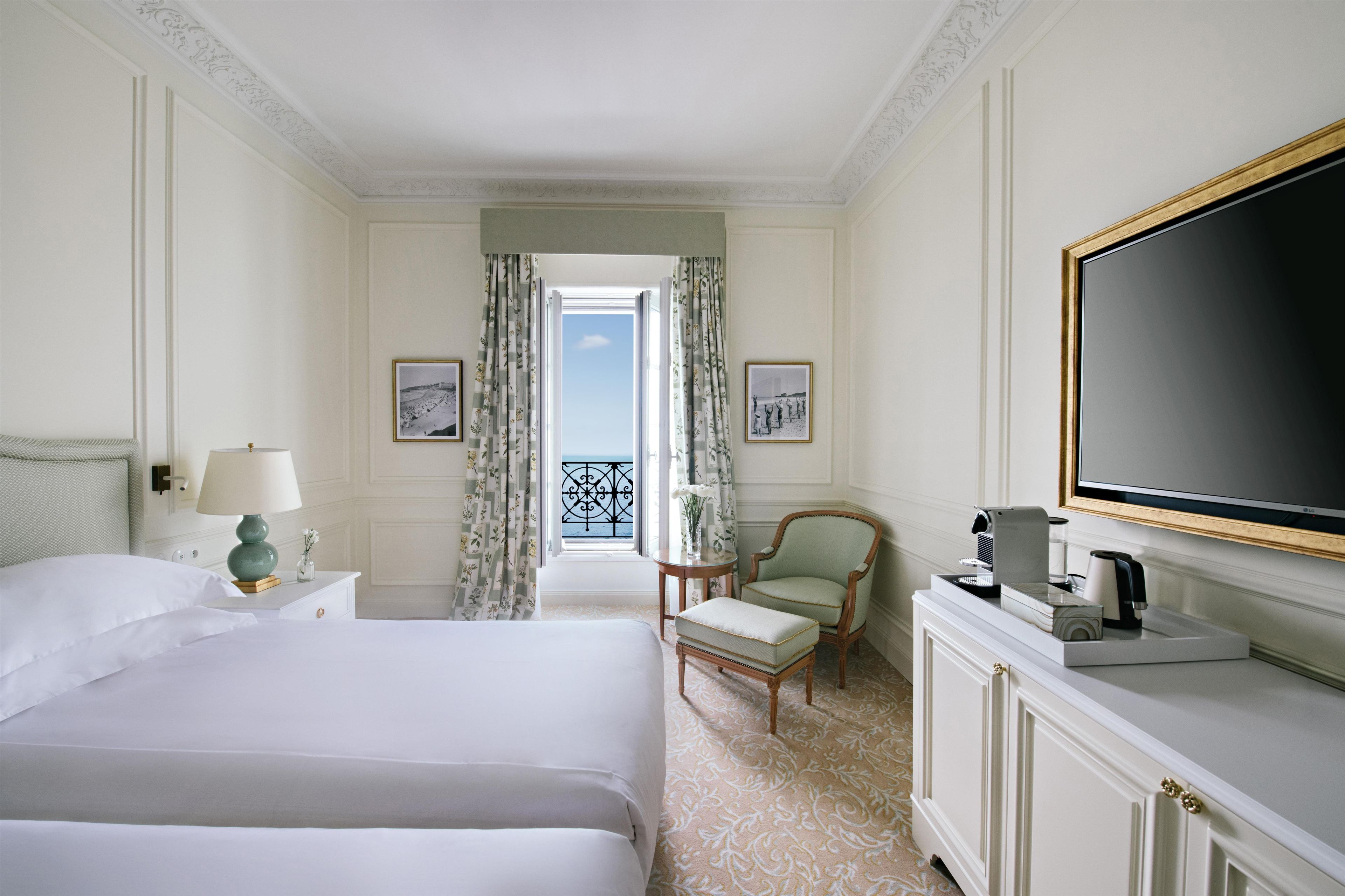 Habitación de hotel con cama, una silla, televisión y vista al cielo a través de la ventana.