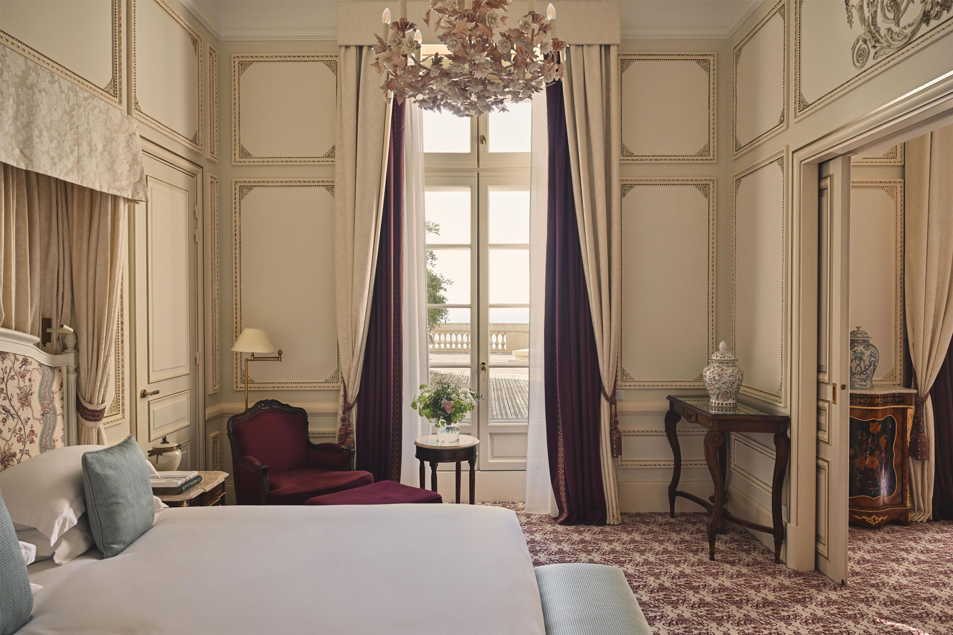 A hotel room with a large bed, a sitting area with a chair, a small table, and a decorative vase.
