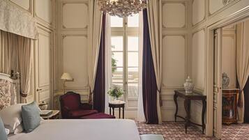 A hotel room with a large bed, a sitting area with a chair, a small table, and a decorative vase.