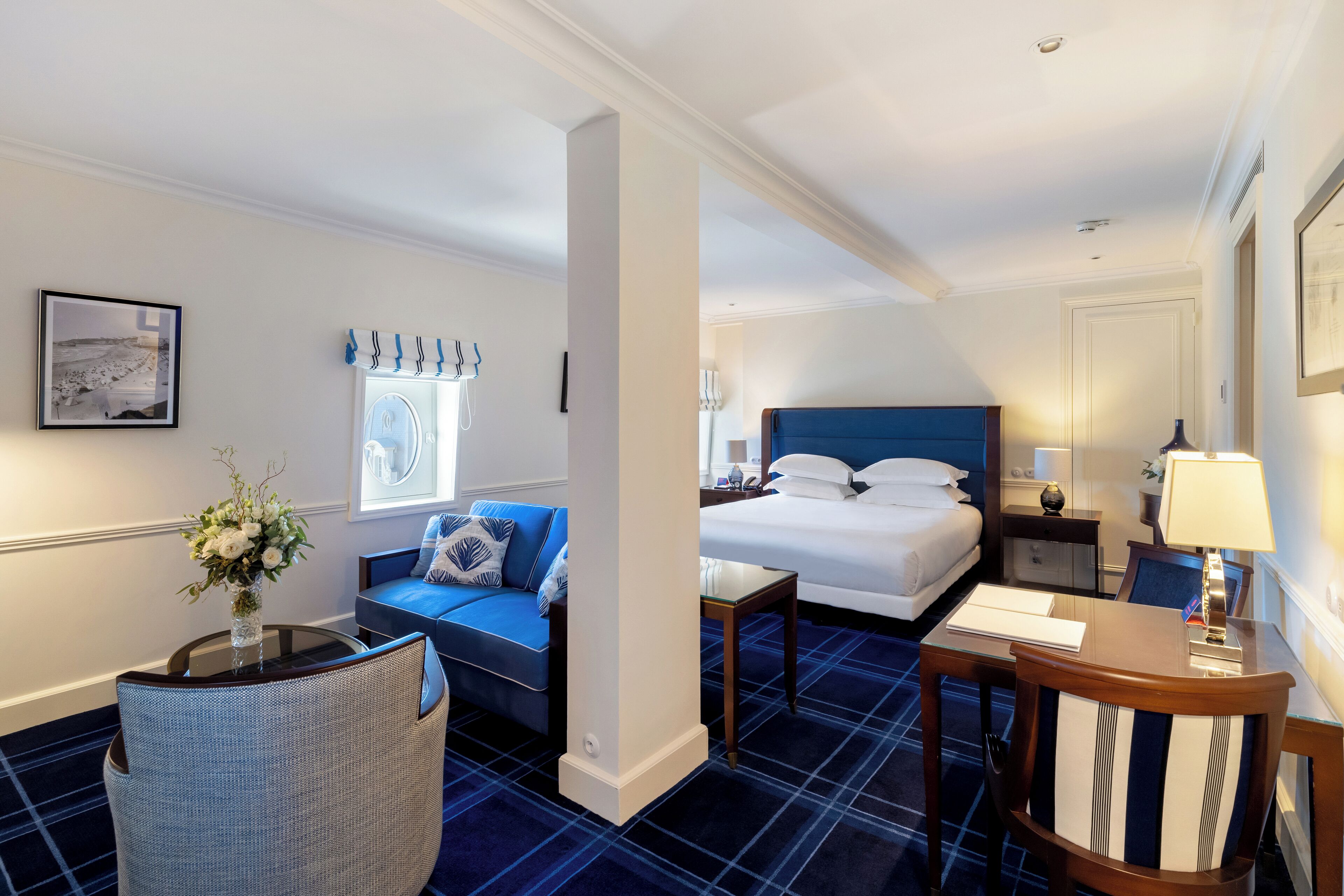 Una habitación de hotel con cama, sofá, sillón, mesita y lámpara.