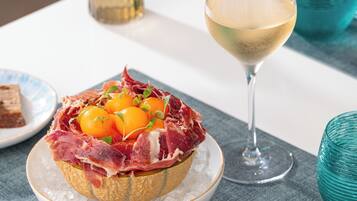A table setting with a glass of white wine, a plate with a meat dish, and a small vase with flowers.
