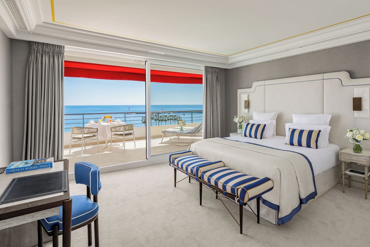 Habitación de hotel con una cama grande, un escritorio y una silla. Se ve el océano a través de las puertas del balcón.