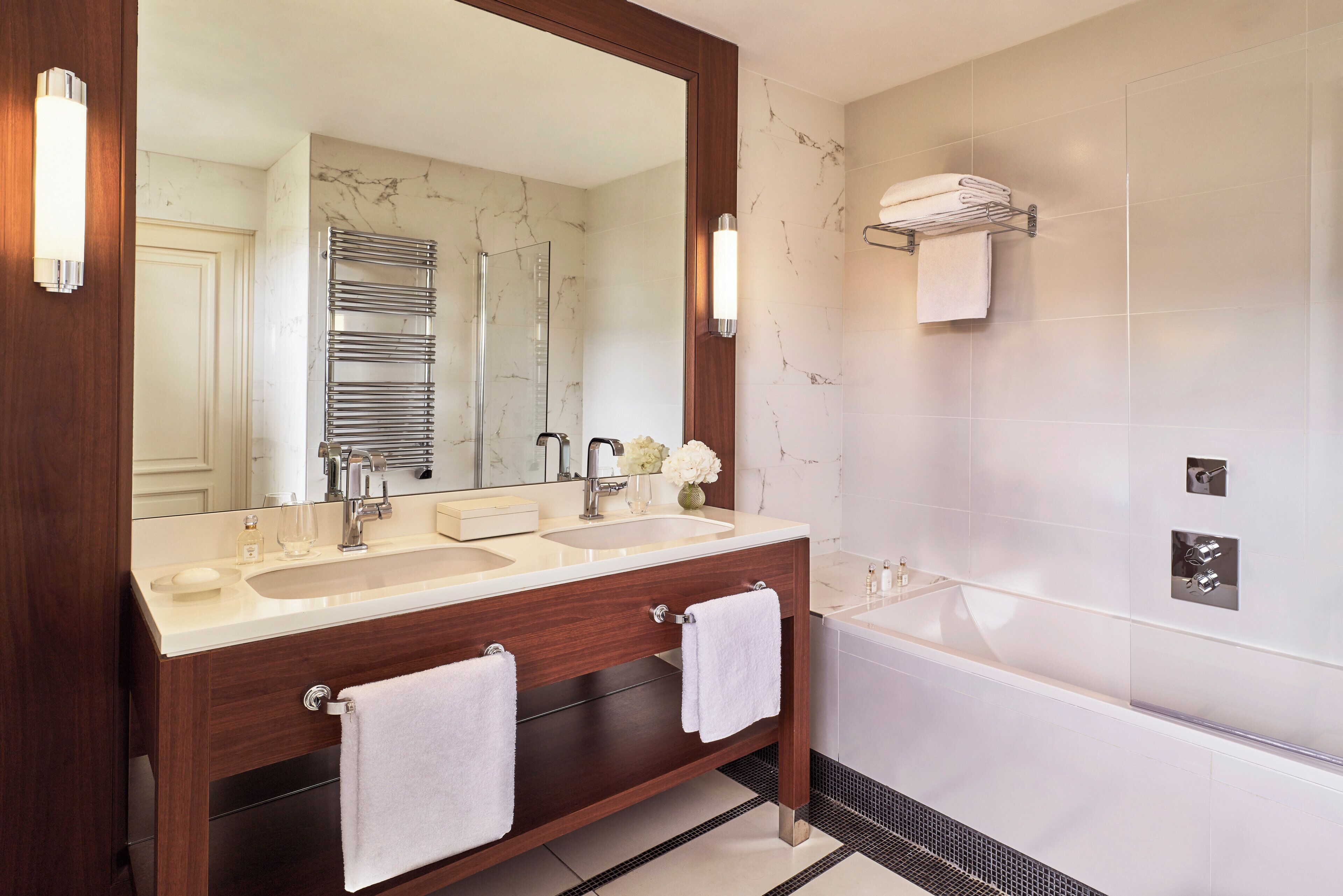 A modern bathroom with a double sink vanity, a large mirror, a glass shower enclosure, and a built-in towel rack.