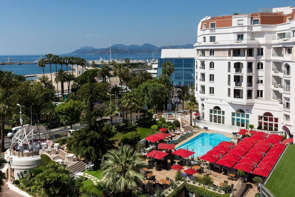 Un hotel con zona de piscina, palmeras y vistas al mar y a las montañas.