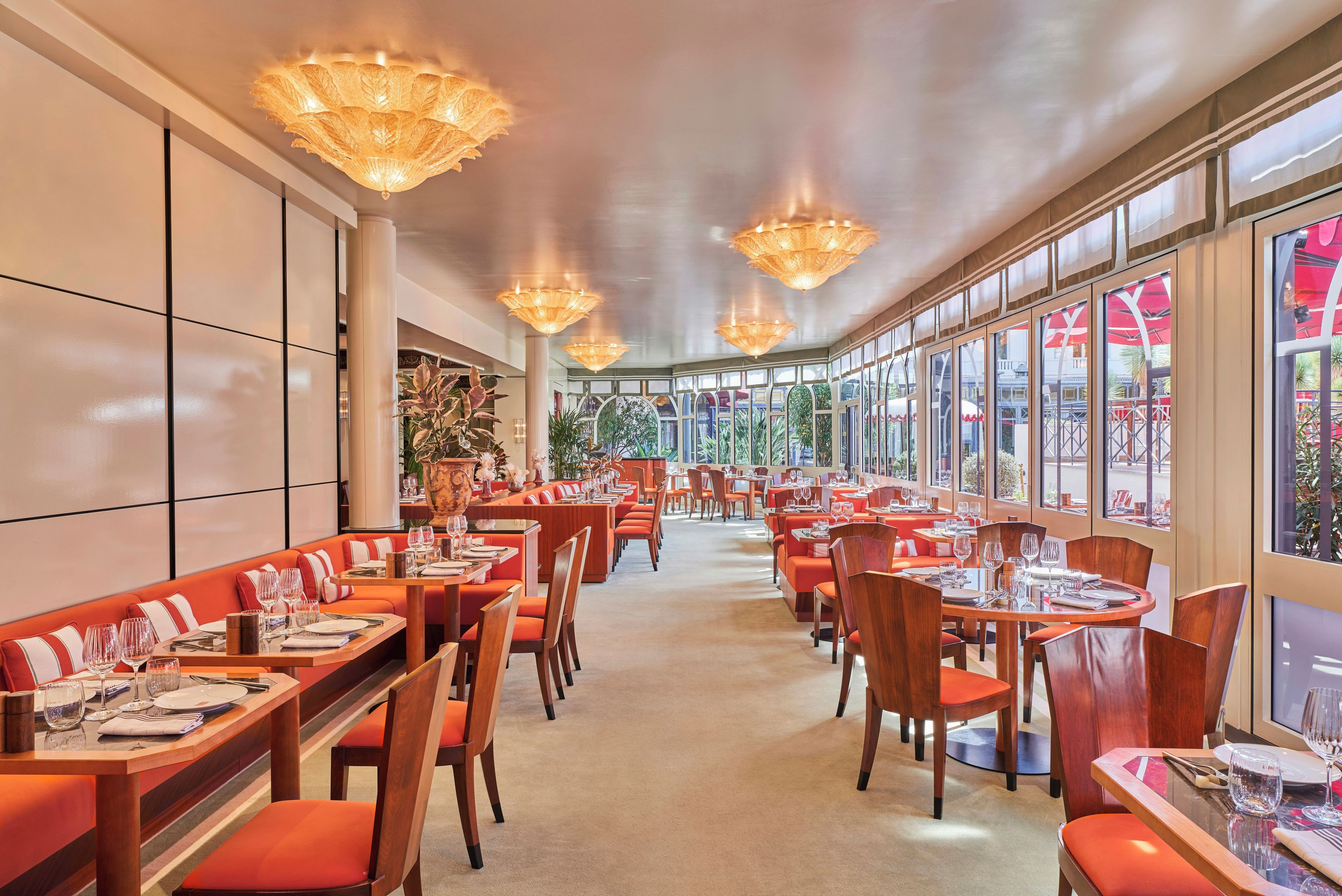 Un restaurante con varias mesas y sillas, ventanas amplias e iluminación decorativa.