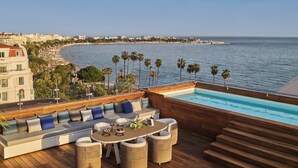 Un área de piscina en la azotea con terraza de madera, asientos y vista a la costa.